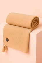 Beige woven blanket with tassels on a pink background, Melo USB heated throw blanket in beige